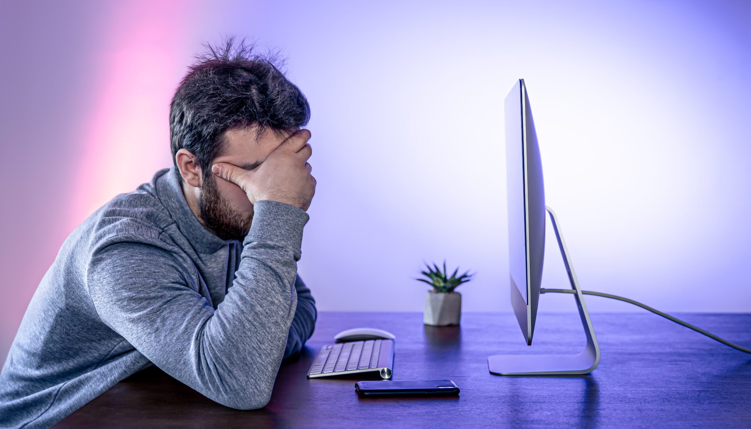 Tired man sits in front of the computer, covered his face with his hands, office work, night work, burnout at work.