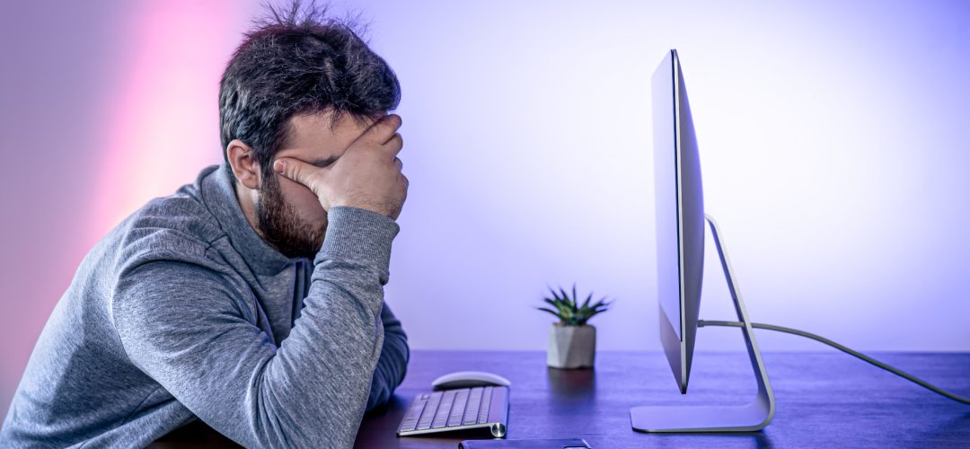 Tired man sits in front of the computer, covered his face with his hands, office work, night work, burnout at work.