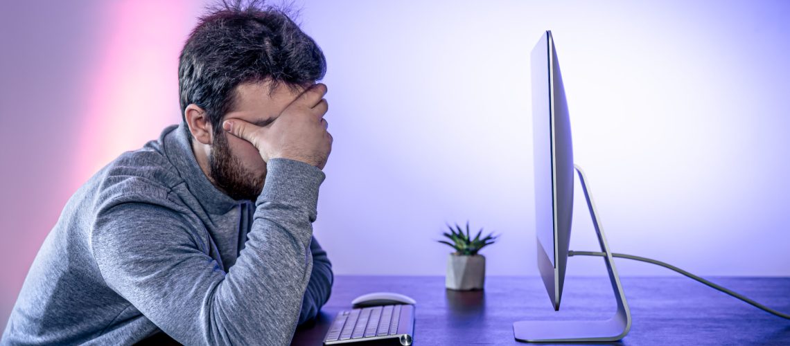 Tired man sits in front of the computer, covered his face with his hands, office work, night work, burnout at work.